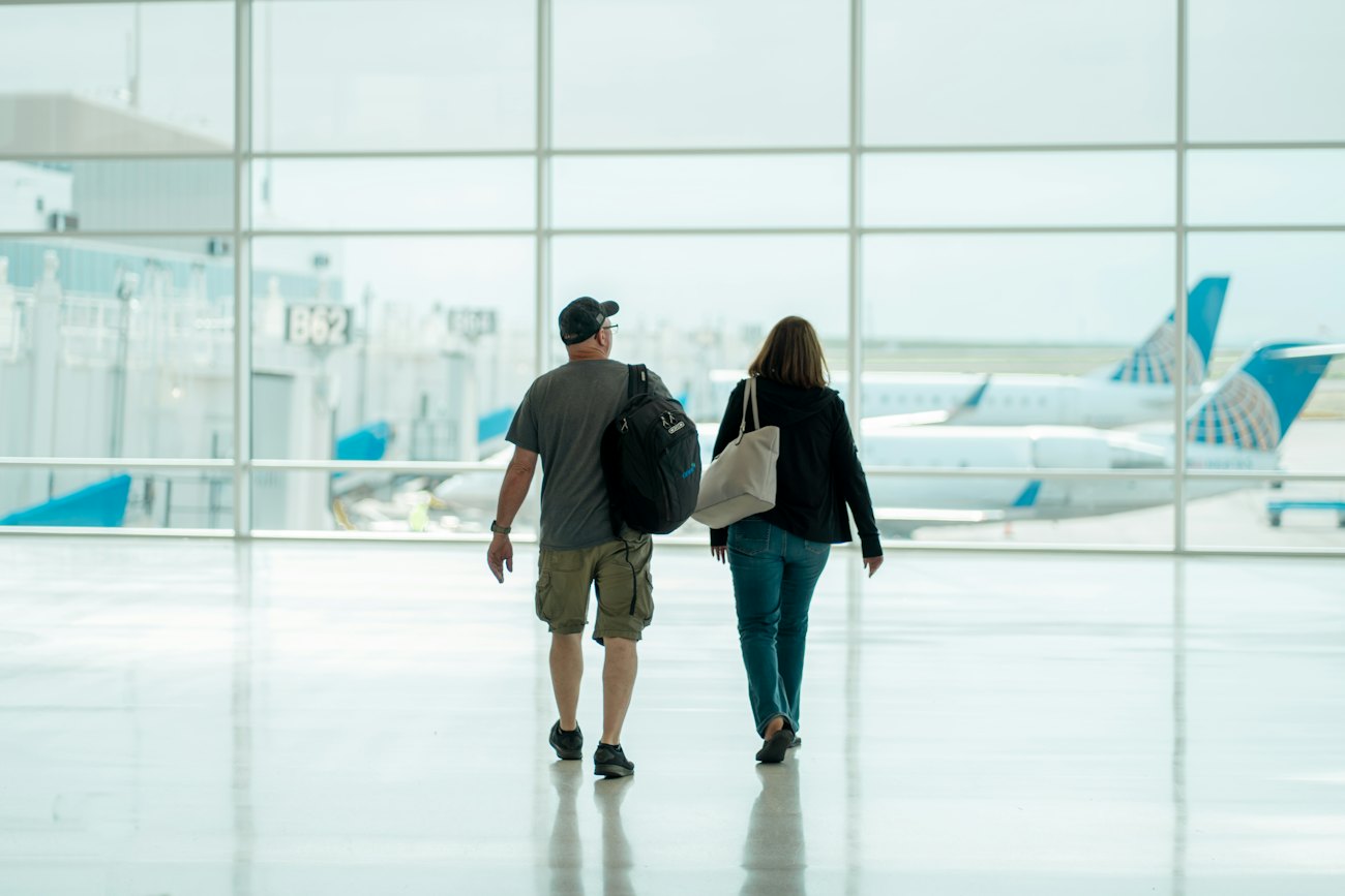 Two travellers with bags walk through a bright airport terminal